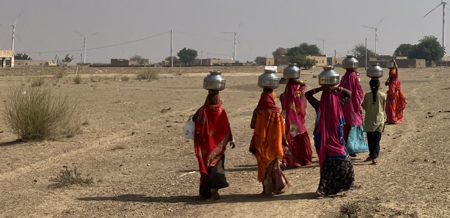 People carrying water through an arid village landscape in Rajasthan